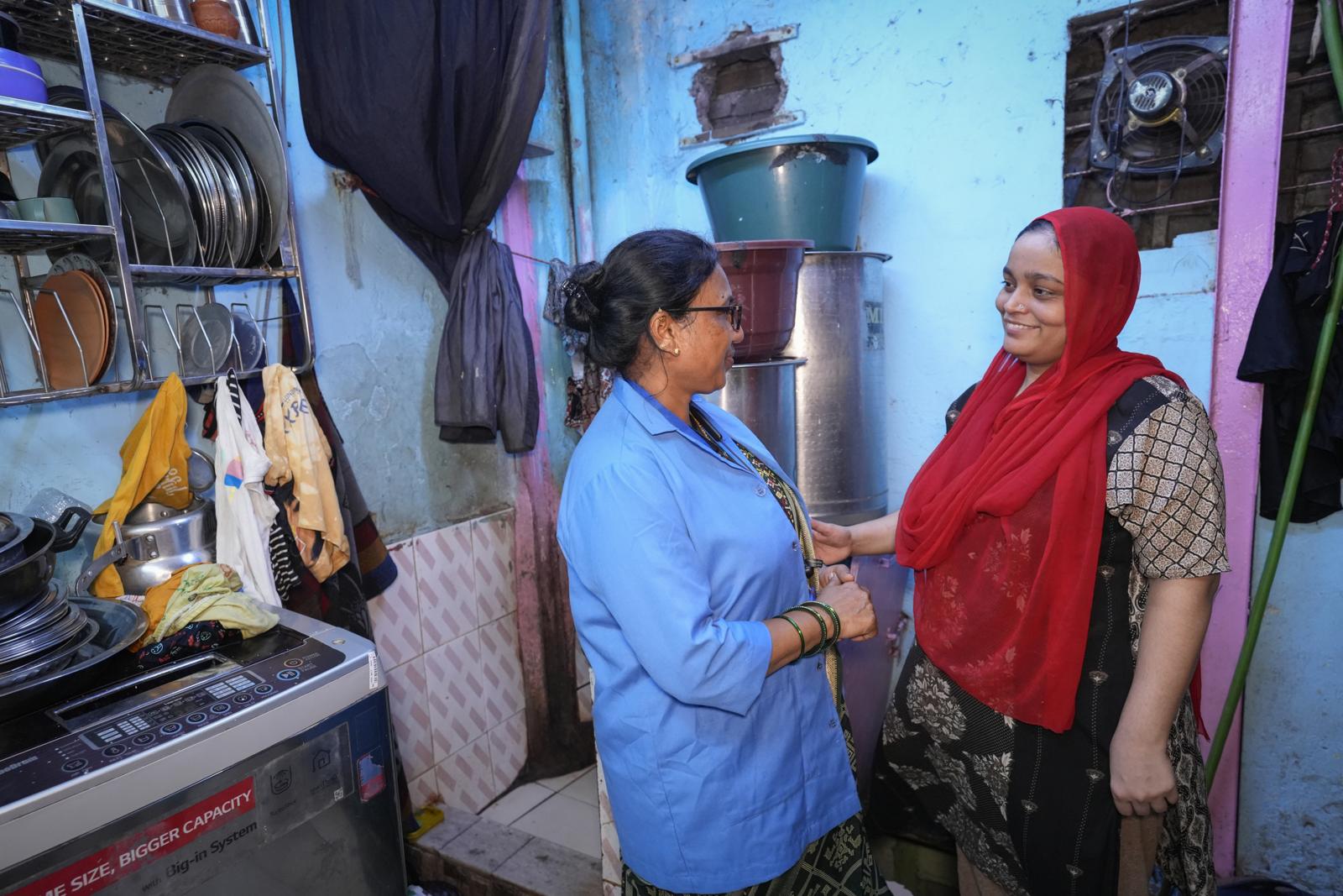 A health worker in a blue coat talking with a woman at the door of her home