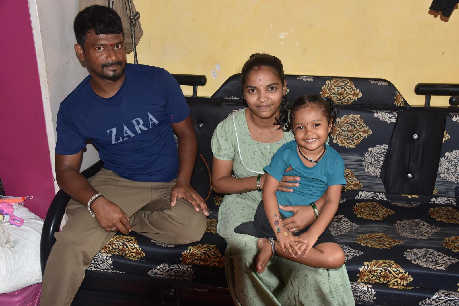 A young family seated together at home, the mother holding her small daughter