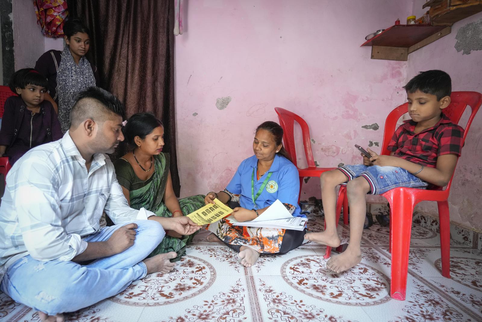 A health worker explaining a leaflet to a family seated on the floor of their home