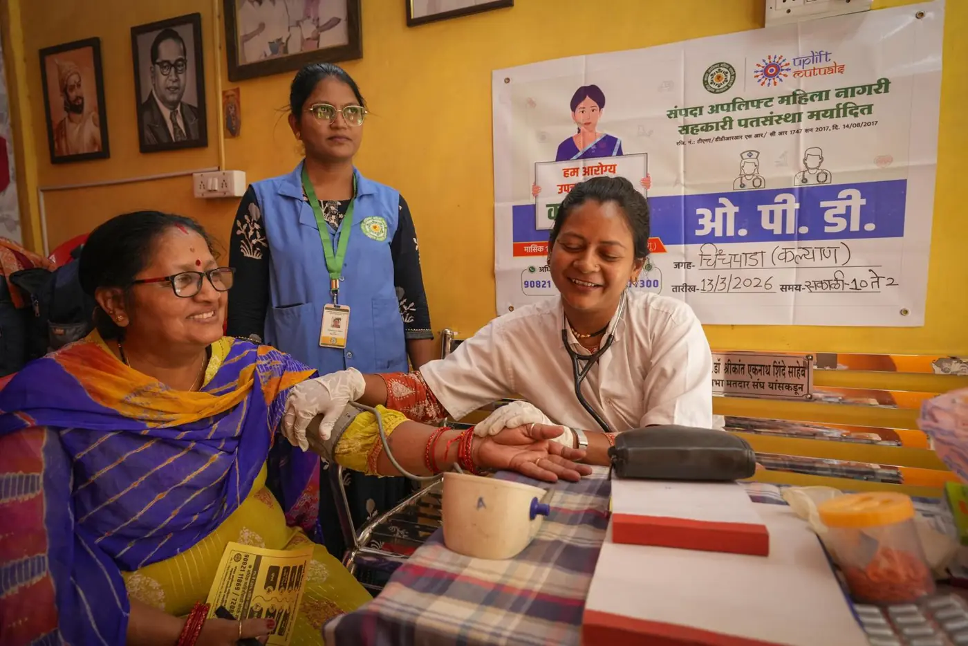 Members at the table during an outpatient session under the Sampada OPD banner, with a community health worker standing behind
